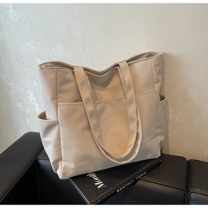 Détail d'un grand cabas beige avec poches avant posé sur un canapé en cuir noir