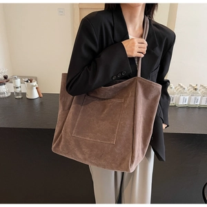Close-up of a large brown suede tote bag featuring a practical front pocket and long strap