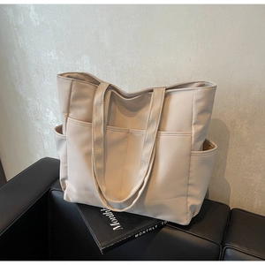 Vue détaillée d'un grand sac fourre-tout beige avec poches sur un canapé noir