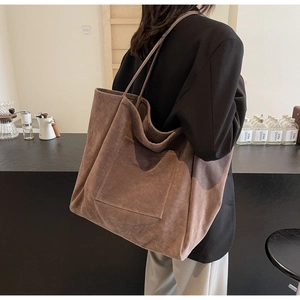 Detail view of large dark brown suede tote bag worn over the shoulder on a casual blazer