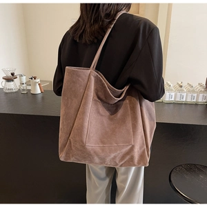 Minimalist large brown suede tote bag shown on shoulder in a cozy cafe setting