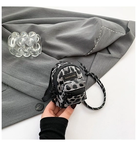 Detail of grey leopard print mini bag featuring a black fashion label and woven strap