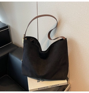 Close-up of black suede texture on bucket bag with brown leather strap and gold hardware