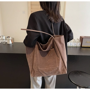Detail of a large brown suede tote bag featuring an outer pocket and minimalist vintage style