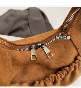 Detail of smooth metal double zippers and pleated suede texture on brown tote bag