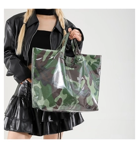 Detail of glossy camouflage tote bag with TOE BAG text worn by model in black outfit