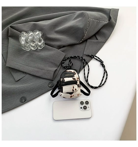 Mini leopard print crossbody bag with cow pattern and rope strap next to a smartphone