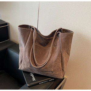 Detail of mocha suede tote bag with front pocket and shoulder straps on magazines