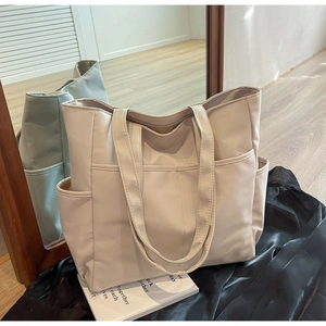 Vue détaillée du sac cabas en toile beige avec plusieurs poches extérieures et doubles anses