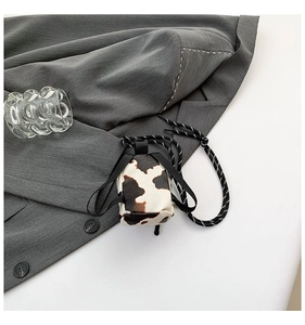 Detailed close-up of mini cow print crossbody bag with woven drawstring on texture fabric