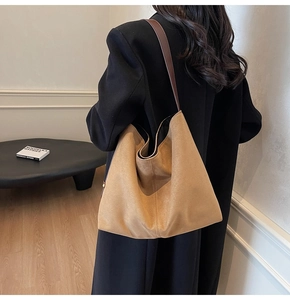 Detail of suede tote bag with brown leather strap over a black wool coat