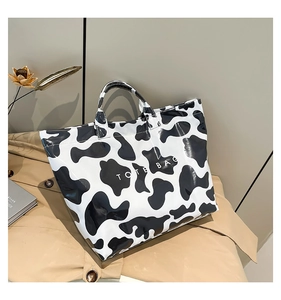 Detail of a high-gloss cow print tote bag placed on a trench coat in a cozy studio setting