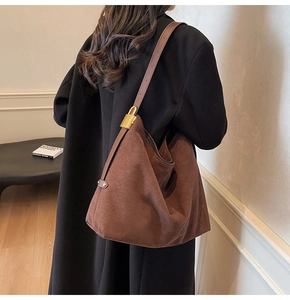 Detail of a brown suede bucket bag featuring a sleek leather strap and gold metal buckle