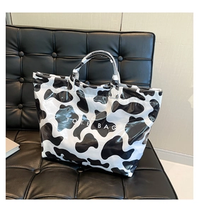 Detail of glossy cow print tote bag with white TOTE BAG lettering on a dark leather sofa