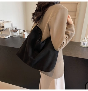 Detail of a large black suede hobo bag with gold metal hardware worn by a model