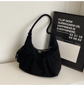 Detail of black suede crescent bag with pleated design on white marble surface