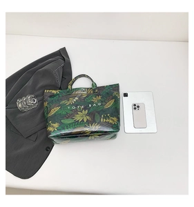 Close-up of green tropical leaf print tote bag with white TOTE BAG lettering and double handles