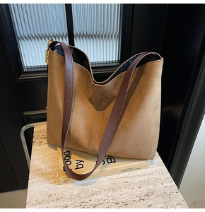 Close-up of brown suede hobo bag with adjustable leather straps on a marble surface