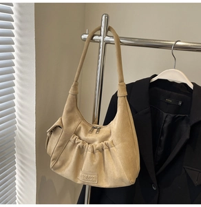 Detail of beige hobo bag with pleated texture and metallic logo on a suede finish surface