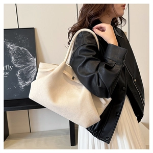 Grande borsa tote scamosciata beige indossata da una modella in giacca di pelle nera chic