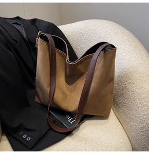 Detail of the suede tote bag with brown leather straps on a white fleece sofa