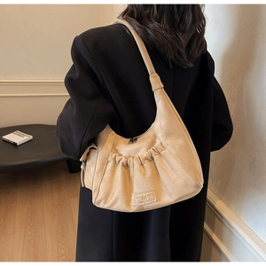 Detailed close-up of beige suede hobo bag featuring pleated design and brand label
