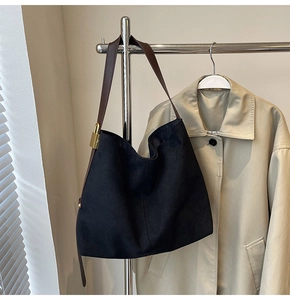 Detail of minimalist black suede tote bag with brown leather strap and gold padlock accessory