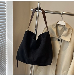 Minimalist black suede bucket bag with brown leather strap hanging in a cozy room setting
