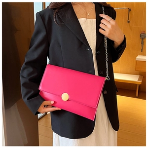 Dettaglio borsa a busta color magenta con catena e grande fibbia rotonda in metallo oro
