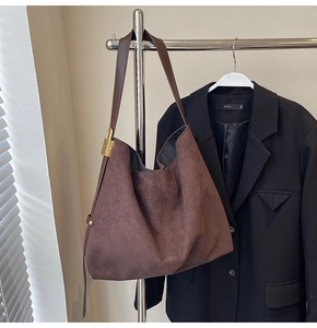 Detail of dark brown suede hobo bag featuring a wide shoulder strap and gold padlock hardware