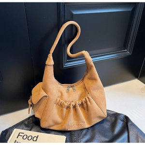 Detail view of brown suede tote bag featuring unique S-curve handles and front pleat pockets