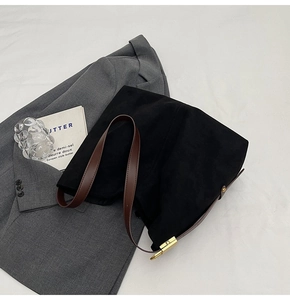 Detail of minimalist black suede bucket bag with brown leather strap and gold buckle