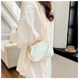Detail of blue and white woven bag with pearl handle and golden chain on a sofa