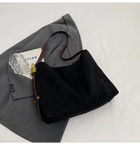 Detail of black suede tote bag with brown leather strap and gold buckle on a blazer
