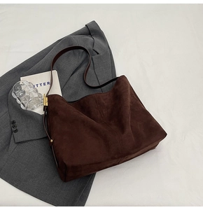 Close-up of dark coffee suede bucket bag on gray suit jacket with gold buckle detail