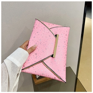 Pochette enveloppe rose à étoiles scintillantes avec bordure dorée tenue à la main sur mur gris