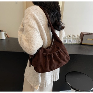 Detail of dark brown suede shoulder bag with pleated texture and leather logo patch