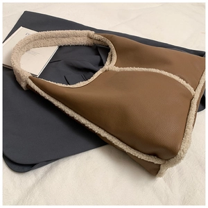 Dettaglio della borsa tote in pelle marrone con bordo in pile beige su abiti grigi