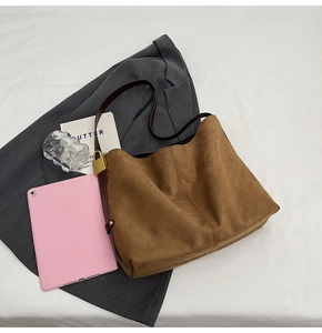 Detail of brown suede tote bag with slim dark straps and golden metal buckle adjustments