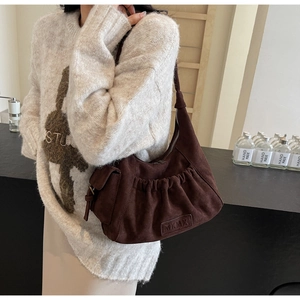 Detail of dark brown suede hobo bag with vintage pleats and leather logo patch