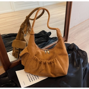 Close-up of brown suede hobo bag featuring MKML logo and side pocket on wooden floor