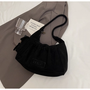 Detail of black pleated shoulder bag with MKMX logo on a grey blazer backdrop