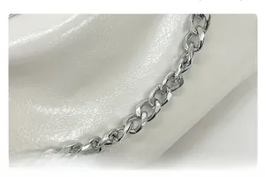Détail d'une bandoulière en chaîne argentée sur une surface en cuir blanc texturé