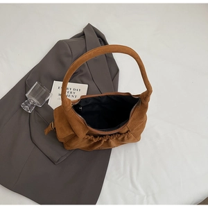 Detail of a brown suede tote bag featuring a pleated base and premium smooth zipper closure