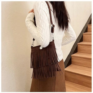 Detail view of dark brown suede crossbody bag with long fringe tassels and metal decor