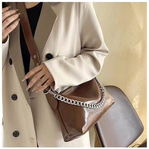 Détail du sac en similicuir marron brillant avec bandoulière large et chaîne argentée