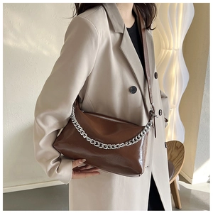 Détail du sac à bandoulière marron brillant avec chaîne argentée sur fond crème