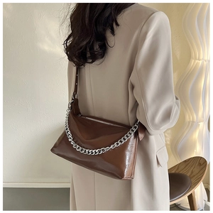 Sac à bandoulière en cuir marron avec chaîne argentée porté par un mannequin en studio