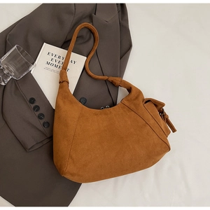 Detail of caramel brown suede hobo bag with side buckle and knotted strap on white fabric