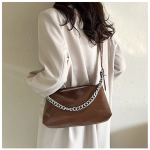 Détail d'un sac en cuir brillant marron avec chaîne argentée sur blazer blanc